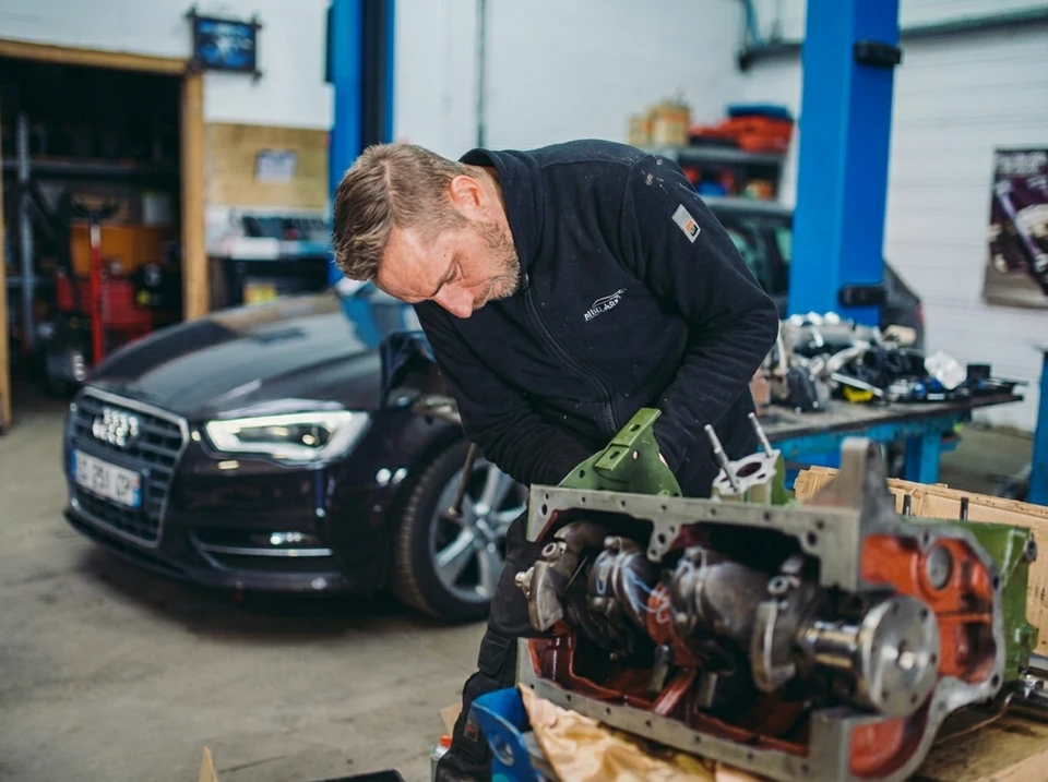 Mécanicien automobile travaillant sous le capot d'un véhicule, remplaçant un filtre à huile dans un garage professionnel