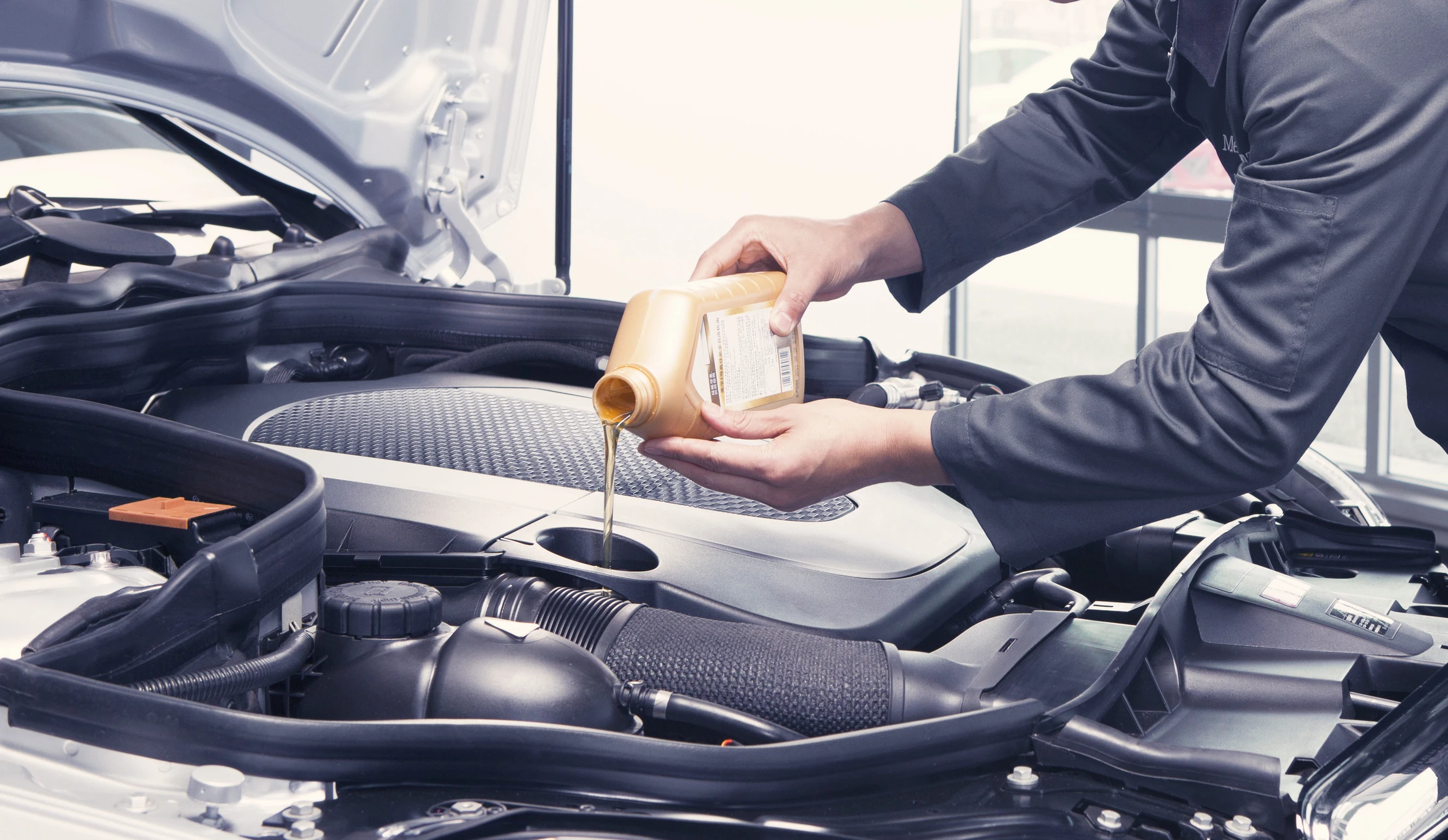 Mécanicien automobile travaillant sous le capot d'un véhicule, utilisant un tournevis pour effectuer une réparation ou maintenance moteur