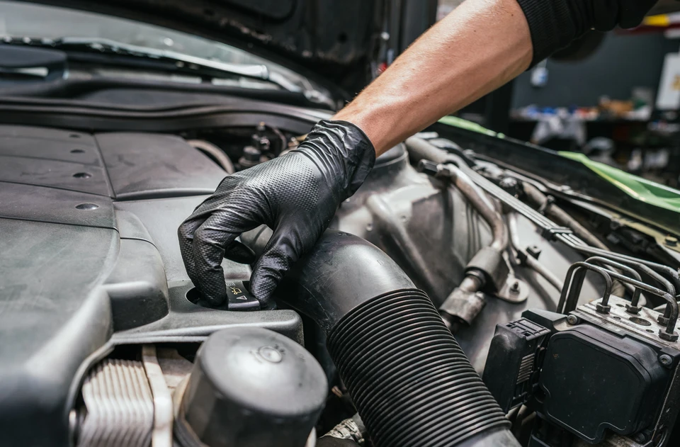 Mécanicien automobile en gants de protection vérifiant le niveau d'huile moteur avec une jauge dans un garage professionnel