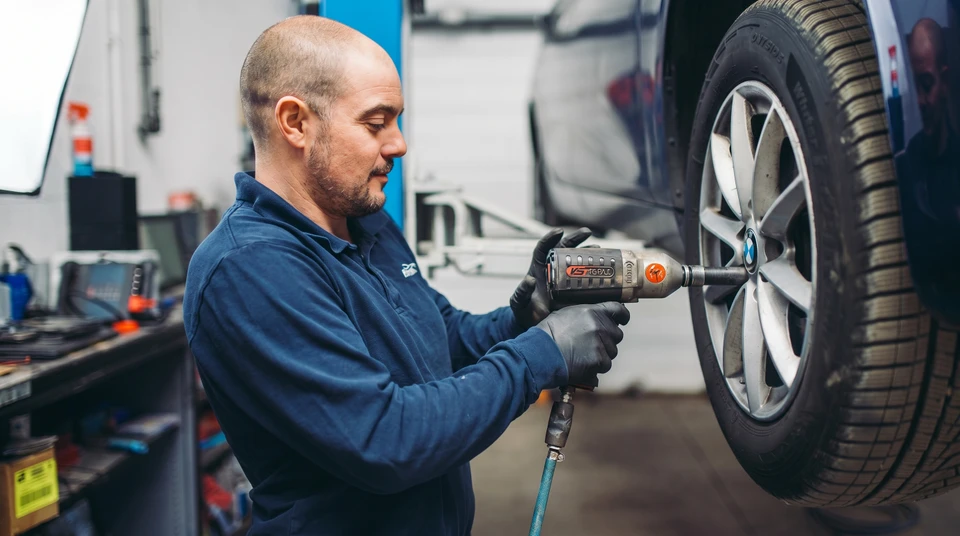 Mécanicien automobile en combinaison bleue gonflant un pneu dans un garage professionnel