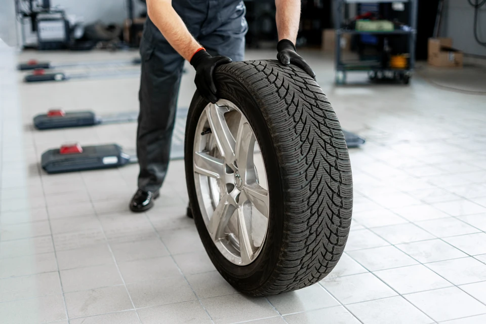 Atelier automobile avec mécanicien en combinaison bleue souriant tenant une tablette numérique, discutant avec un client en chemise à carreaux