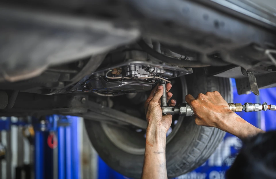 Mécanicien automobile travaillant sous un véhicule surélevé dans un garage professionnel, effectuant des réparations avec outillage spécialisé